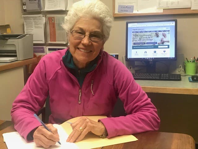 A volunteer counselor at a desk with the Medicare website on the screen.