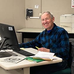 A smiling tax volunteer at a desk with a computer and paperwork.